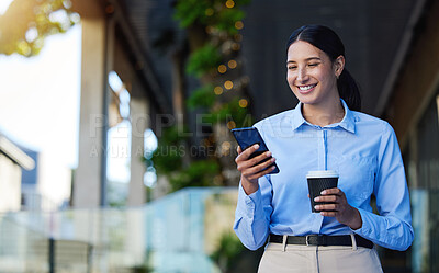 Young mixed race happy businesswoman using social media on a phone while drinking a cup of coffee. One hispanic woman smiling while typing a message on her phone and standing in the city