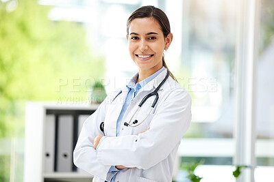 Confident young mixed race female doctor standing with her arms crossed inside a medical office. One hispanic woman in a white coat with stethoscope. Trusted practitioner caring for the health of patients