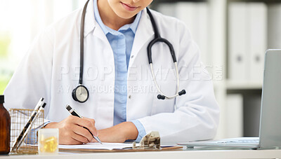Closeup of an unknown doctor sitting alone in her clinic and writing notes. Female doctor writing in her notebook in office at the hospital