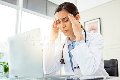 Closeup of a young mixed race doctor looking worried and suffering from a headache while working on a computer in her office. Hispanic female suffering from a head pains and stress at a hospital