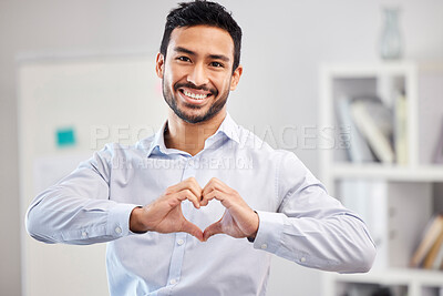 Buy stock photo Young happy handsome mixed race businessman making a heart gesture with his hands standing in an office alone at work. One hispanic male boss smiling showing love and support with a hand gesture

