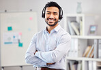 Young happy mixed race call center agent standing with his arms crossed in an office at work. One hispanic customer service agent wearing a headset and answering calls while standing in an office