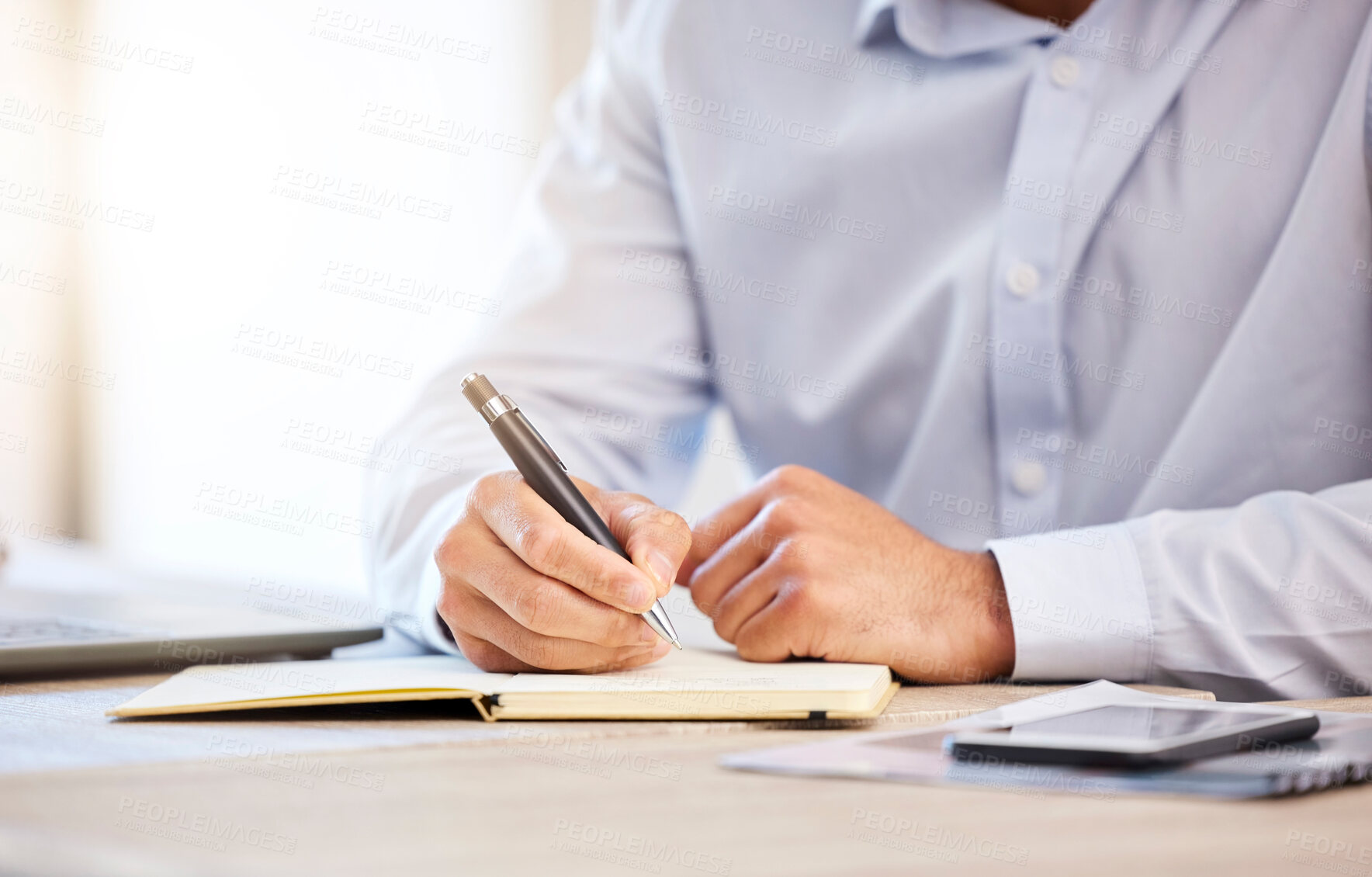 Buy stock photo Unknown businessman writing notes while using in an office. Mixed race man holding a pen and writing in a notebook