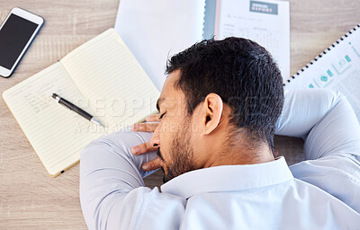 Businessman sleeping on a table from above. Tired young man having a nap on his desk at work in a modern office. Top view of an exhausted employee suffering from stress and burnout in the workplace