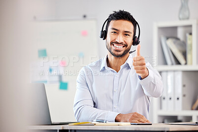 Young happy handsome mixed race male call center agent showing a thumbs up wearing a headset sitting at a desk in an office alone at work. Pleased hispanic customer service agent answering calls