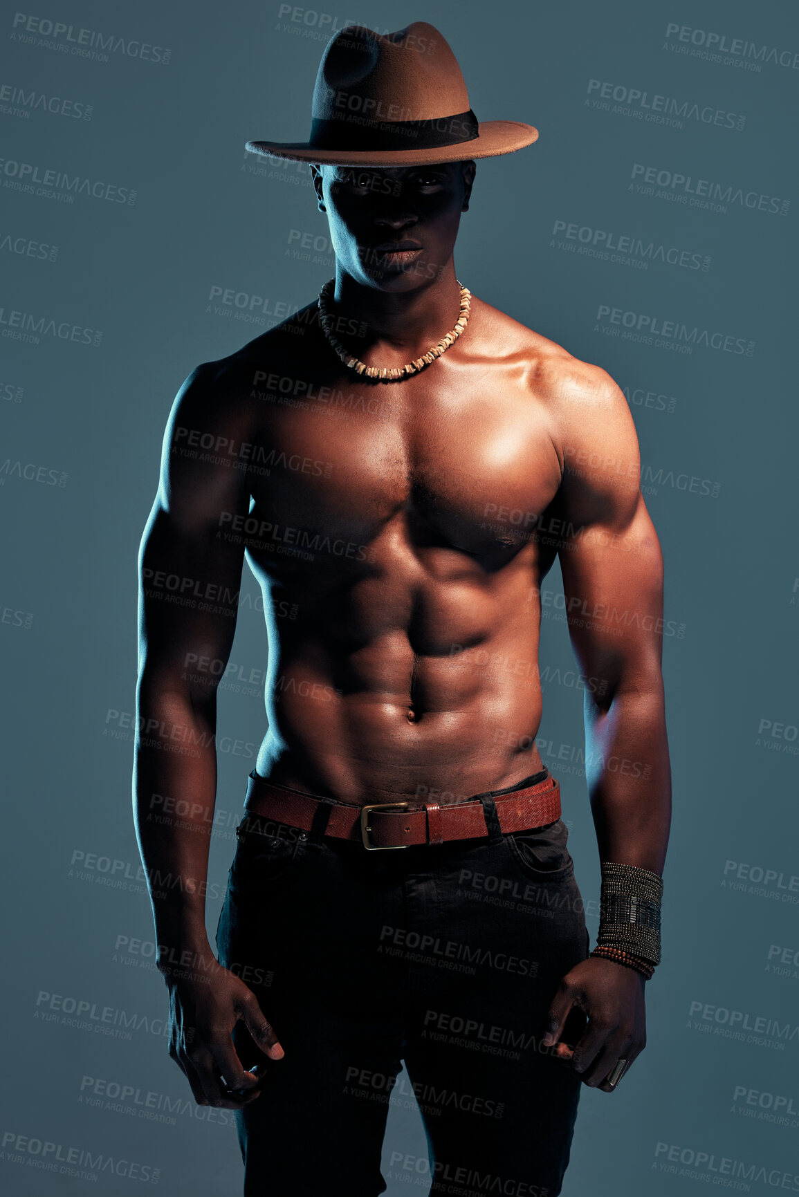 Buy stock photo Black man, shirtless with strong fashion model and sexy, cow boy style with hat isolated on blue background. Dark, shadow and body with muscular male person, pose with six pack and stylish in studio