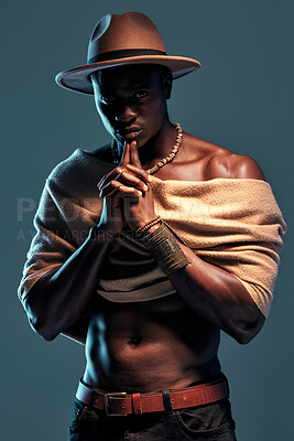 Fashionable african American model posing with wrapped scarf against blue studio background with copyspace. Serious black man with attitude thinking while wearing hat and shawl. Masculine and muscle