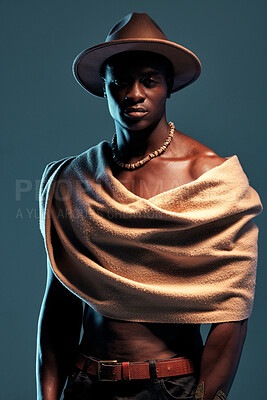 Fashionable african American model posing with wrapped scarf against blue studio background with copyspace. Sexy, serious, handsome black man with attitude wearing hat and shawl. Masculine and muscle
