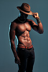 Fashionable african American model posing shirtless against blue studio background with copyspace. Sexy, serious black man with attitude showing bare six pack while wearing hat. Masculine and muscle