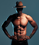 Fashionable african American model posing shirtless against blue studio background with copyspace. Sexy, serious black man with attitude showing bare six pack while wearing hat. Masculine and muscle