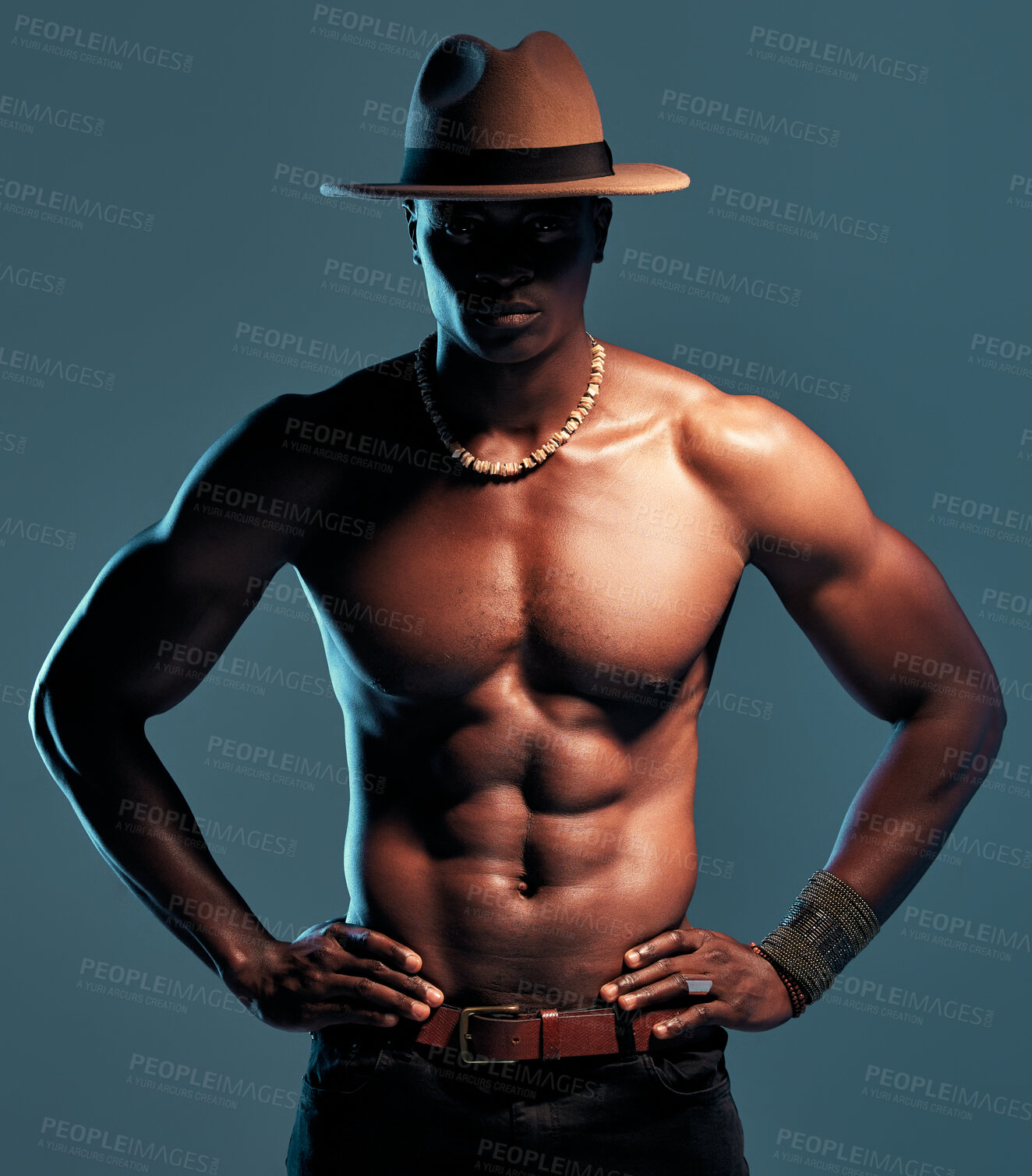 Buy stock photo Black man, shirtless and fashion, sexy model with abs and cow boy style with hat isolated on blue background. Dark, shadow and body with muscular male person, pose with six pack and stylish in studio