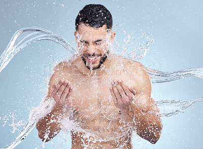 Studio closeup of a handsome young man splashing water on his face against a grey studio background. Hispanic male enjoying and smiling during a shower