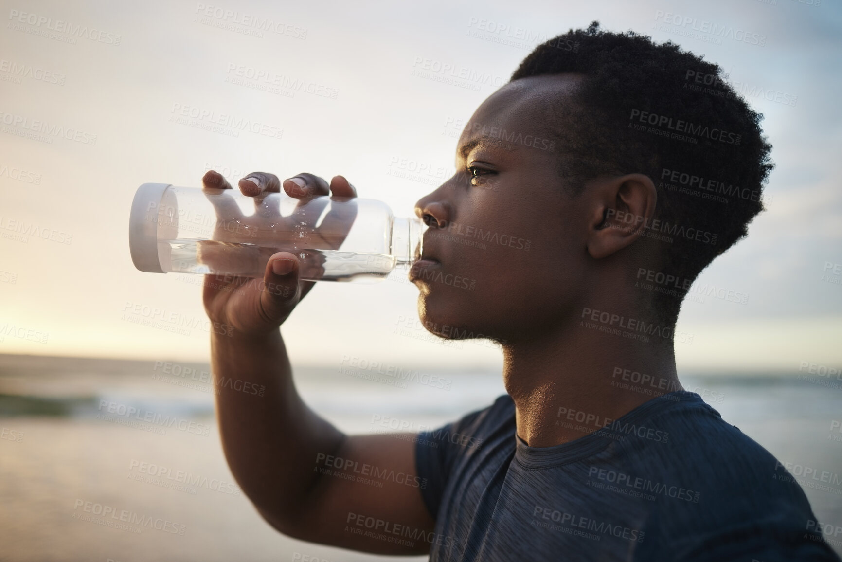 Buy stock photo Black man, beach fitness and drinking water at sunset on running break, exercise or workout. Drink, liquid and African male athlete with bottle for nutrition, hydration or health, wellness and ocean.