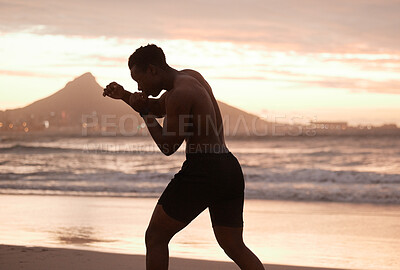 One african american man practicing shadow boxing on a beach at sunset. Black male focus on speed, strength and fitness while showing his muscular athletic shape against a sunrise copyspace background