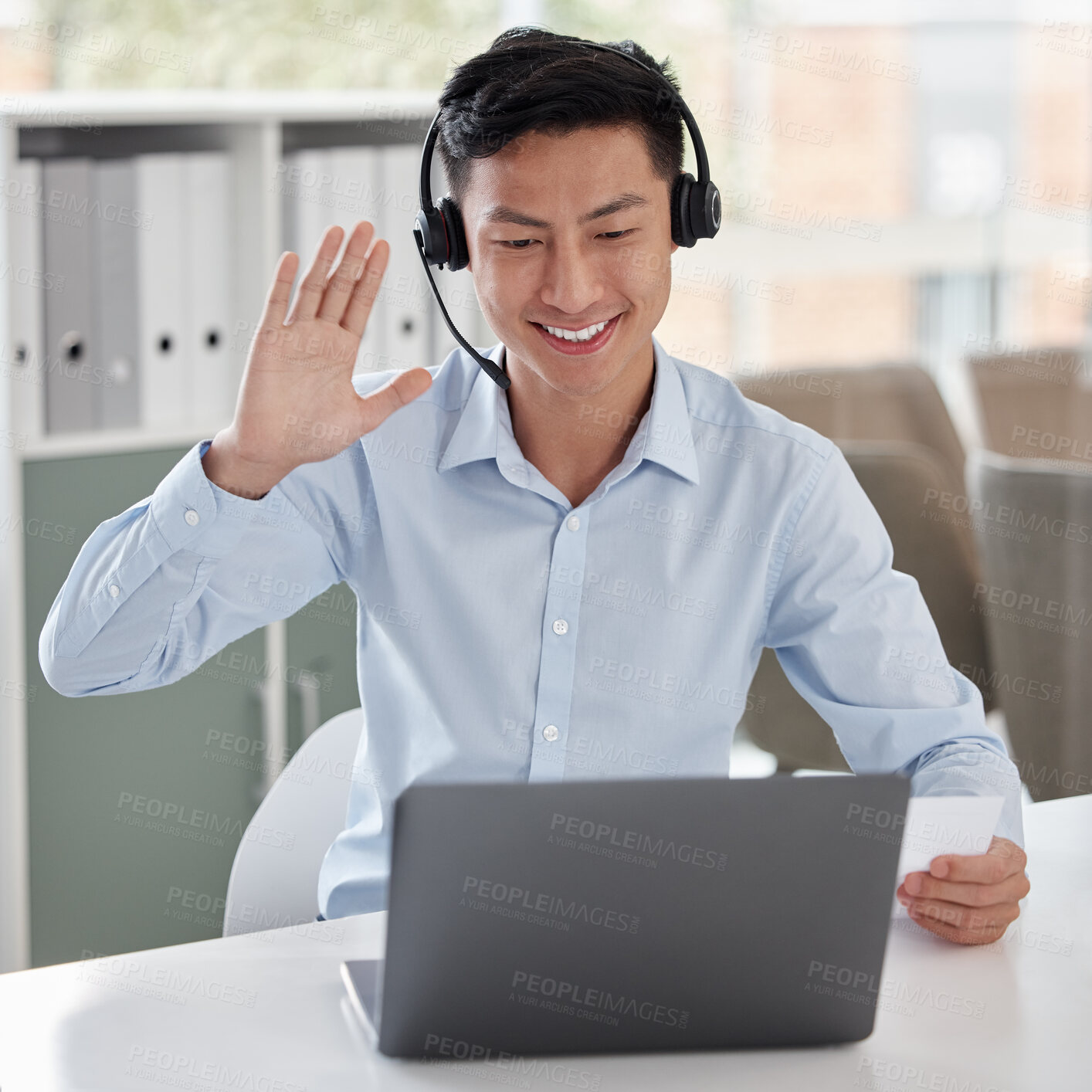 Buy stock photo One happy asian businessman talking on headset and waving to greet colleagues during virtual teleconference meeting via video call on laptop in an office. Advisor and rep joining online global webinar