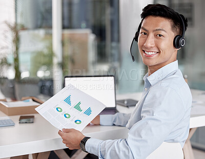 Buy stock photo Asian businessman working in a call center reading a document. Financial advisor wearing a headset. Customer service rep reading paperwork. Businessman looking at finance reports. Marketing rep on a call in front of a laptop