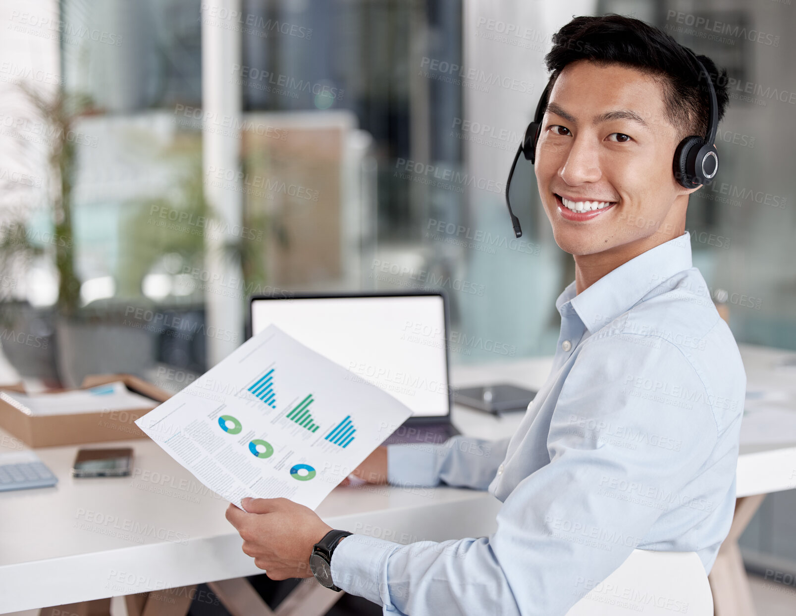 Buy stock photo Asian businessman working in a call center reading a document. Financial advisor wearing a headset. Customer service rep reading paperwork. Businessman looking at finance reports. Marketing rep on a call in front of a laptop