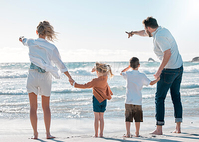 Buy stock photo Back of family on holiday at the beach. Family pointing to the distance on the beach. Caucasian family on vacation by the sea. Parents bonding with their children on a getaway.