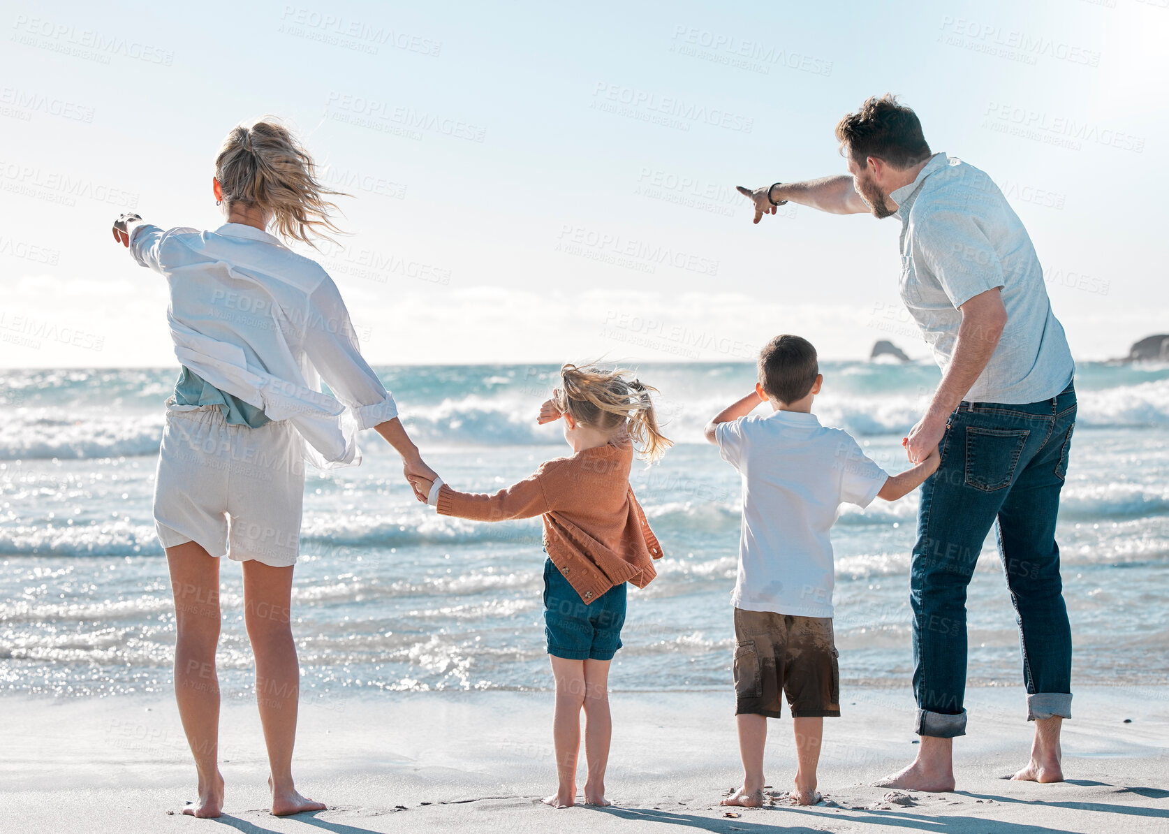 Buy stock photo Back of family on holiday at the beach. Family pointing to the distance on the beach. Caucasian family on vacation by the sea. Parents bonding with their children on a getaway.