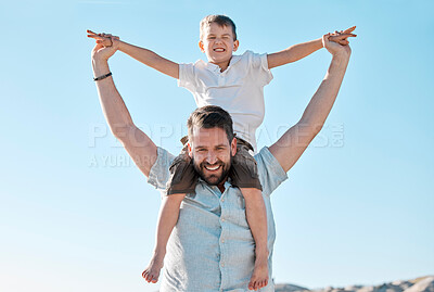 Portrait of happy caucasian father and playful son having fun in the sun against blue sky outside. Carefree man carrying excited boy on shoulders piggyback ride and pretending to fly with arms out