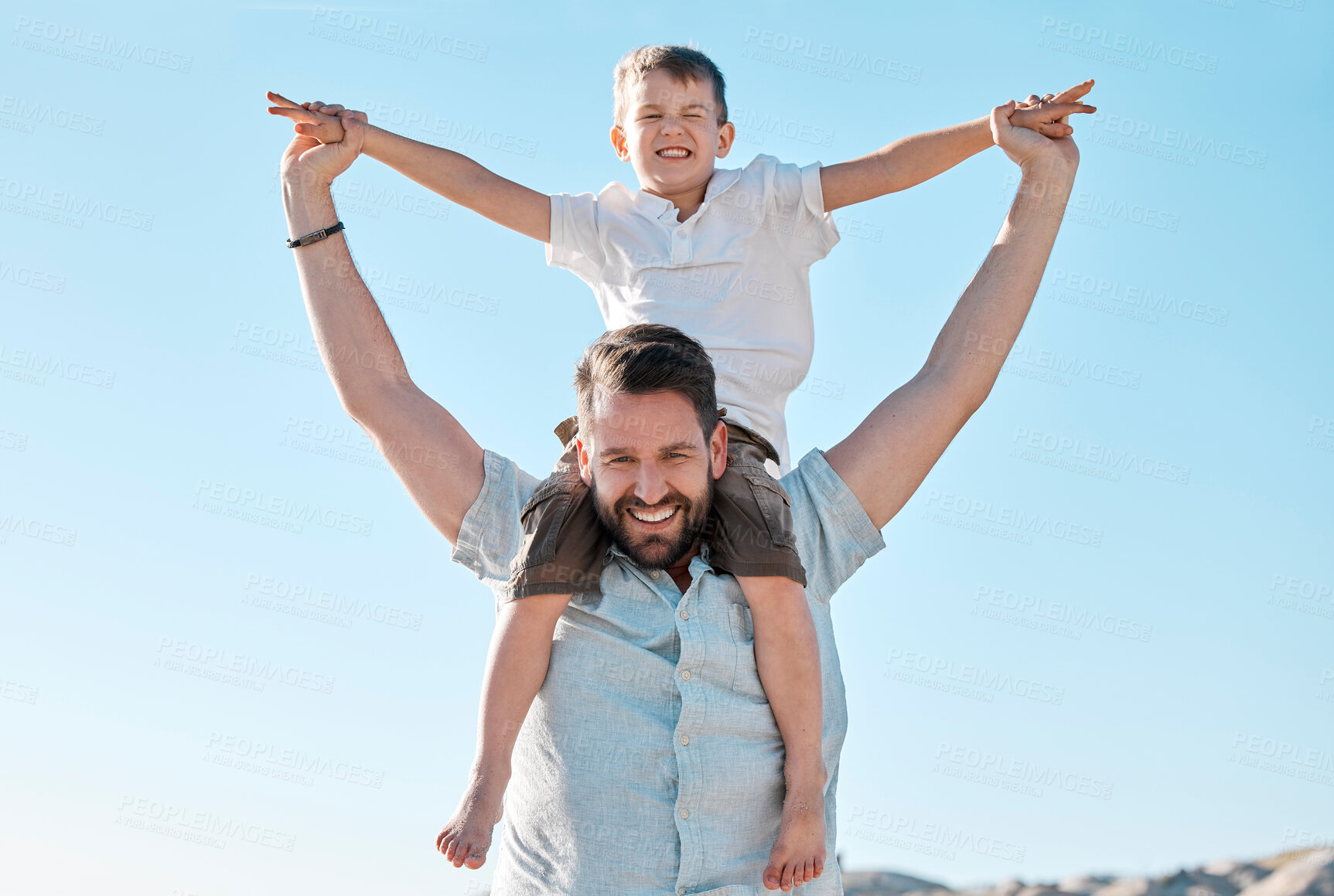 Buy stock photo Portrait of happy caucasian father and playful son having fun in the sun against blue sky outside. Carefree man carrying excited boy on shoulders piggyback ride and pretending to fly with arms out