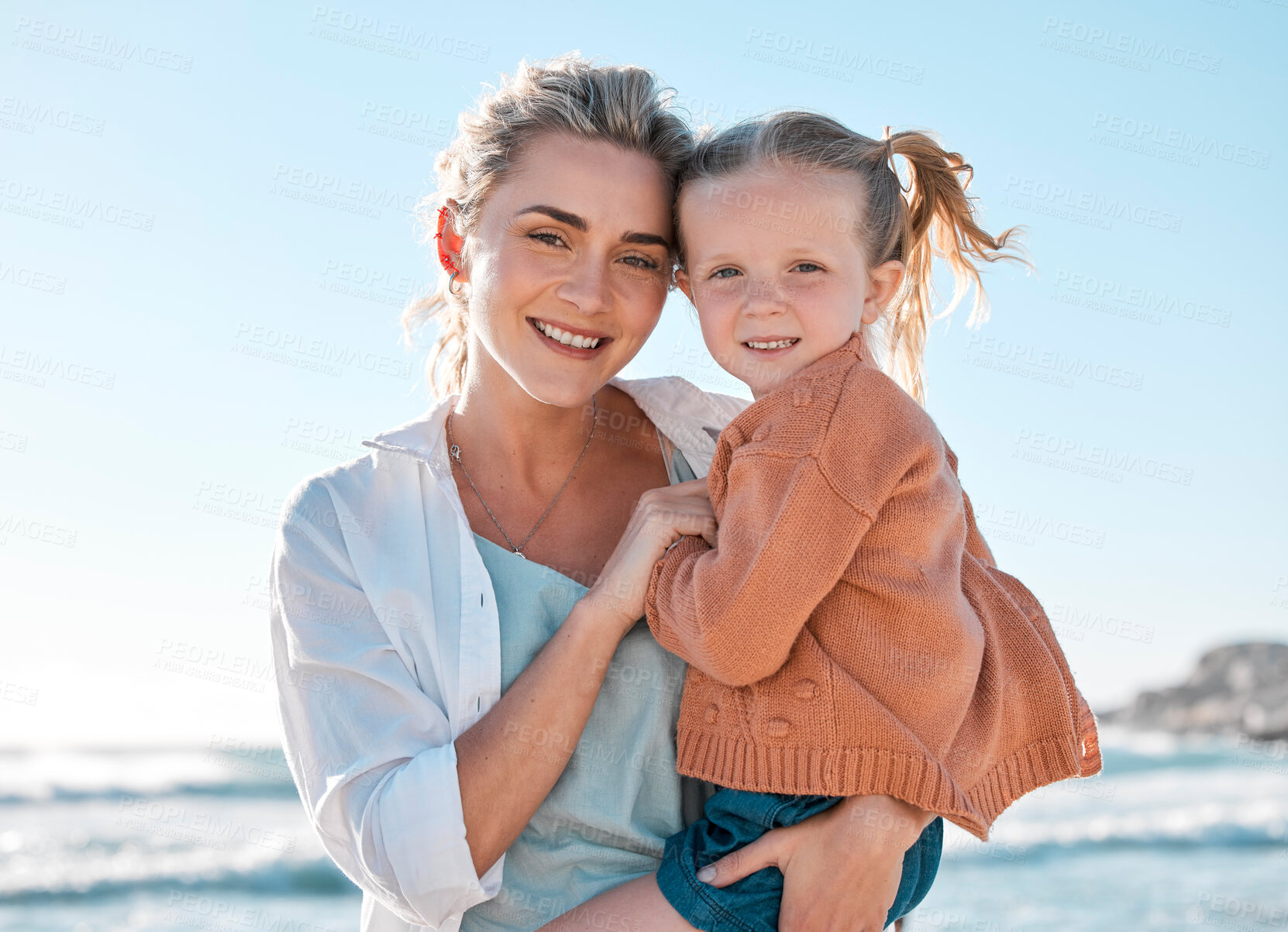 Buy stock photo Portrait of happy caucasian mother holding cheerful daughter while having fun in the sun at beach. Smiling woman carrying carefree girl while bonding outside. Loving mom enjoy quality time with kid