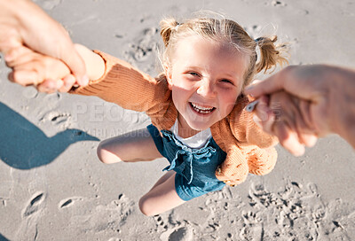 Happy caucasian girl swinging and spinning in circles by the arms at the beach shore with her father. Face of cute playful kid having fun while bonding with a parent on sunny summer vacation outdoors