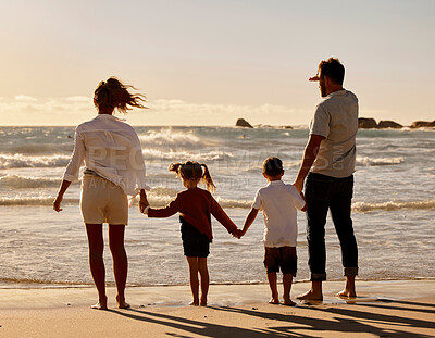 Back of caucasian parents with son and daughter enjoying free time on a beach. Little boy and girl holding hands and bonding with their mother and father on the weekend. Family watching the sunset