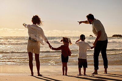 Buy stock photo Rear view of family on holiday at the beach during sunset. Mother and father pointing to the distance on the beach with son and daughter. Caucasian family on vacation by the sea. Parents bonding with their children on a getaway.