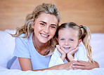 Portrait of happy caucasian mother and daughter lying on bed at home. Cheerful woman with little girl enjoying a cosy and lazy relaxing day. Loving parent bonding and sharing quality time with kid