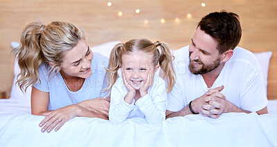 Happy parents with little daughter lying on bed at home. Smiling caucasian girl bonding and enjoying free time with her mother and father on the weekend. Young husband and wife with their only child