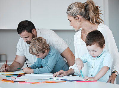 Buy stock photo Young caucasian family sitting together at home. Loving parents helping their little children with homework. Carefree siblings focused while writing in notebooks with their mom and dad