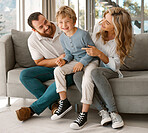 Happy relaxing caucasian family of three smiling while sitting and bonding on the sofa together. Adorable little blonde boy chilling on a couch with his loving parents and playfully laughing with them