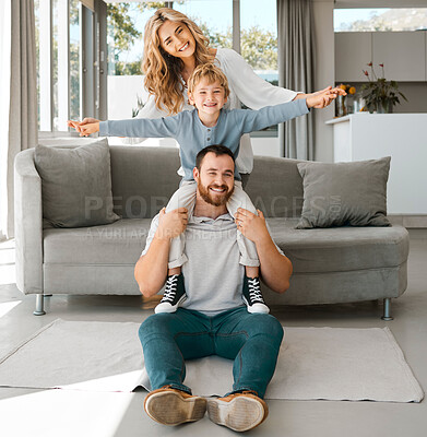 Portrait of a happy family. Parents and son at home. Adorable caucasian boy smiling and sitting on his father\'s shoulders with arms outstretched. Young husband enjoying time with his wife and son