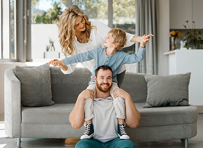 Portrait of happy parents and little son at home. Adorable caucasian boy smiling and sitting on father\'s shoulders with arms outstretched pretending to fly. Young parents enjoying free time with son