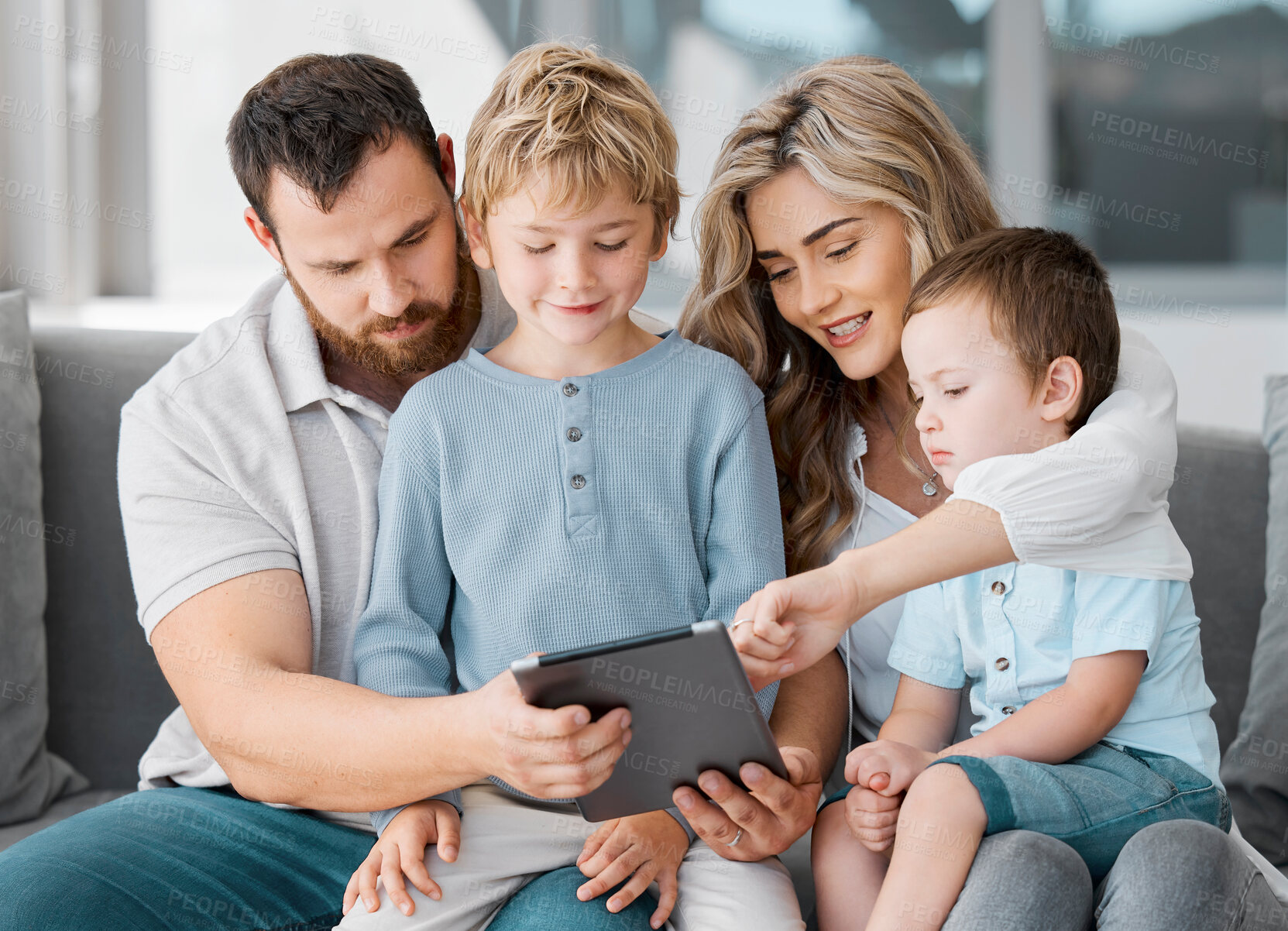 Buy stock photo Happy relaxed family of four using a digital tablet device while bonding on the sofa together at home. Young couple checking social media and watching a movie with their two cute caucasian sons