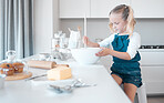 Little girl mixing a bowl of batter. Young child baking alone in the kitchen. Little girl sitting at her kitchen counter. Caucasian girl holding a mixing bowl. Young child baking at home.
