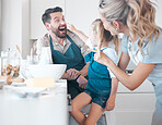 Playful caucasian family baking together. Little girl putting flour on her fathers nose. Cheerful young family enjoying cooking together. Little child playing and baking with her parents.