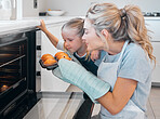 Young mother smelling a tray of fresh baked muffins. Caucasian woman sniffing a tray of muffins. Mother and daughter removed fresh baked muffins from the oven. Woman enjoying the smell of muffins