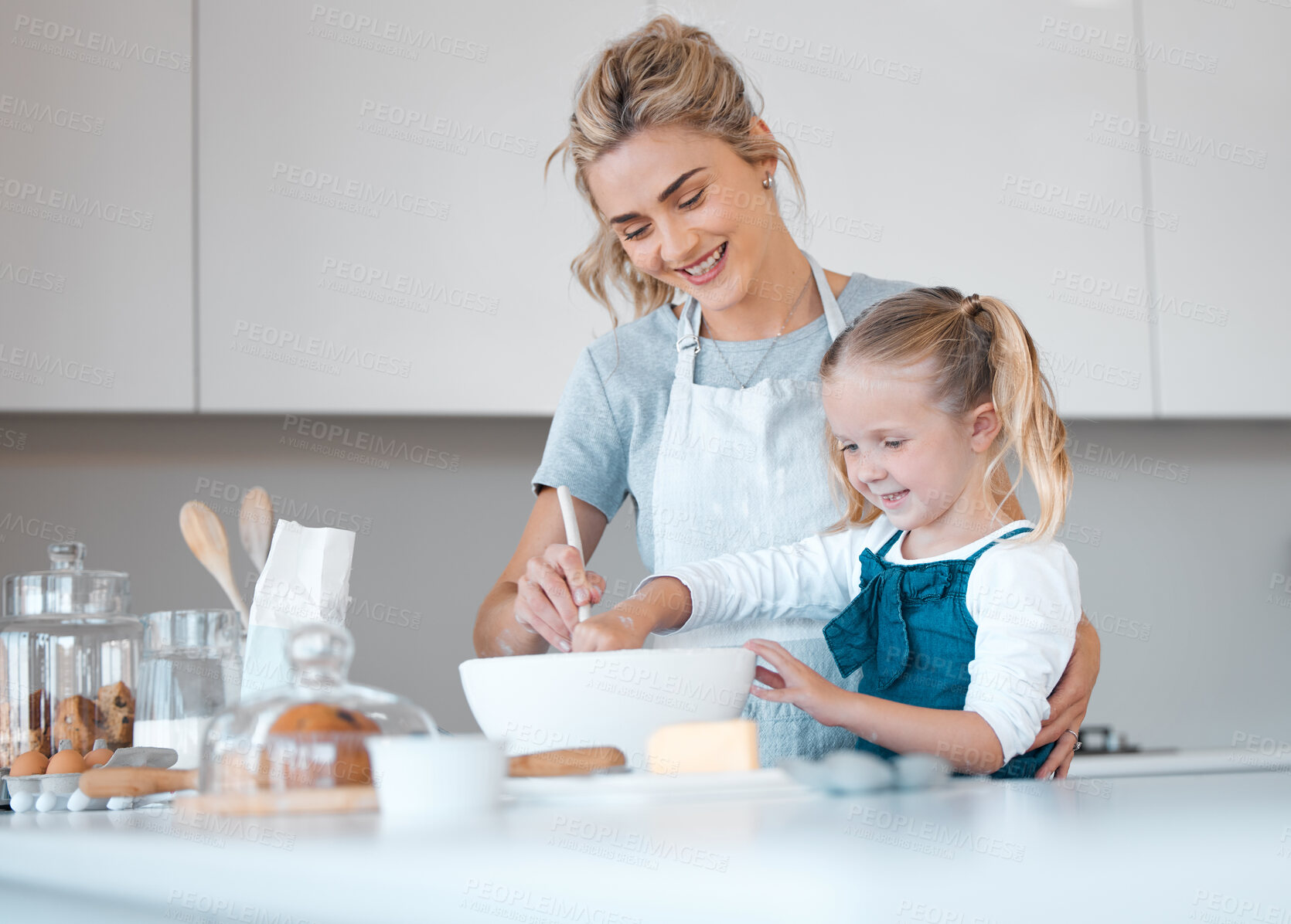 Buy stock photo Happy mother helping her daughter bake. Parent baking with her child. Young woman helping her daughter make batter. Little girl mixing a bowl of batter. Smiling family baking in the kitchen