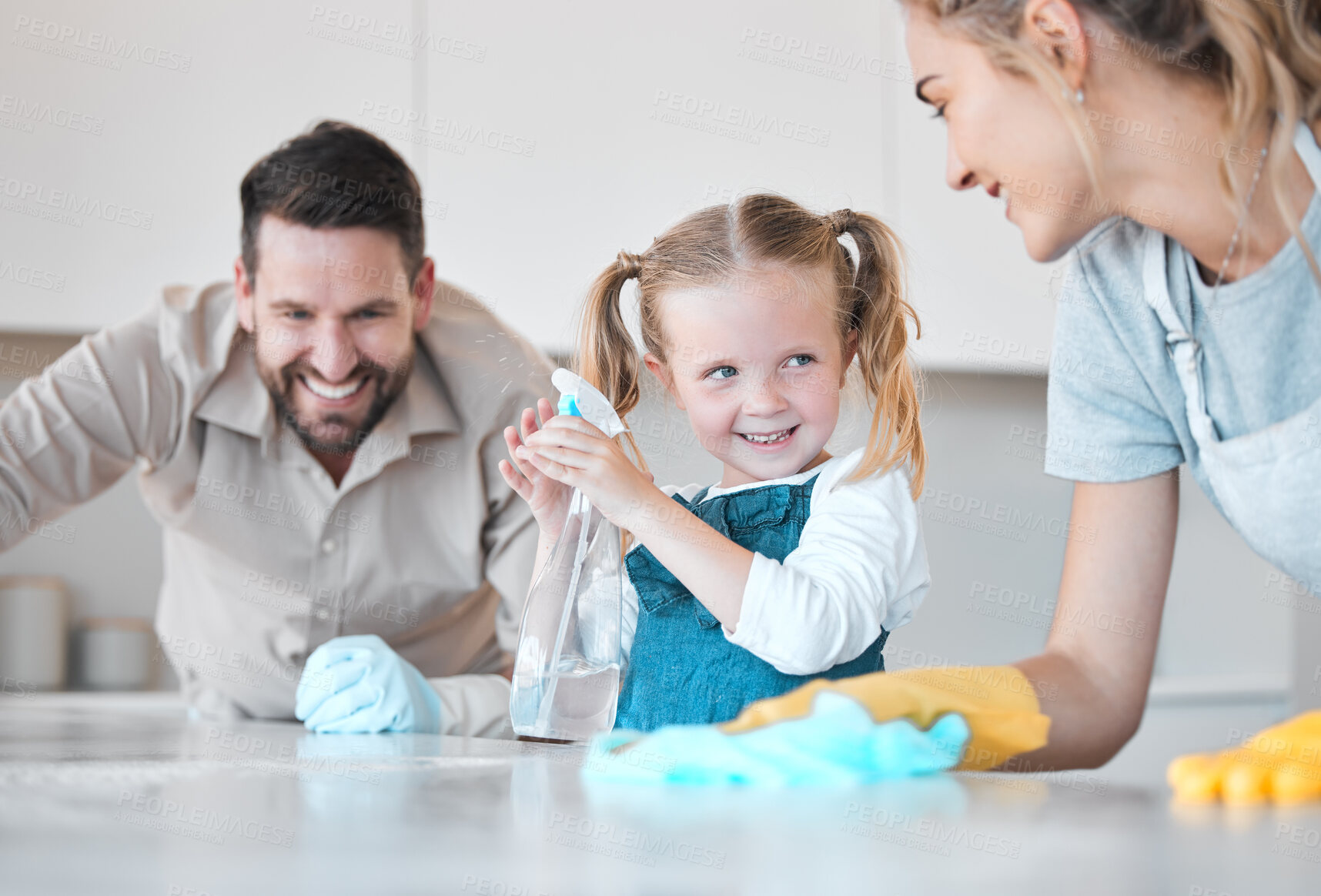 Buy stock photo Happy family cleaning the kitchen together. Little girl spraying disinfectant from a bottle. Caucasian family cleaning the kitchen counter together. Mother and father bonding with their daughter