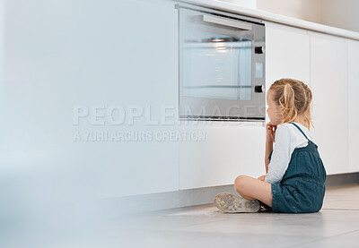 Little girl patiently waiting by the oven. Caucasian child sitting and looking at the oven door. Little child waiting for her baked foods. Blonde little girl sitting on her kitchen floor