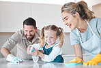 Little girl spraying the kitchen counter. Caucasian family cleaning the kitchen together. Happy family doing chores together. Cheerful family disinfecting the kitchen counter together