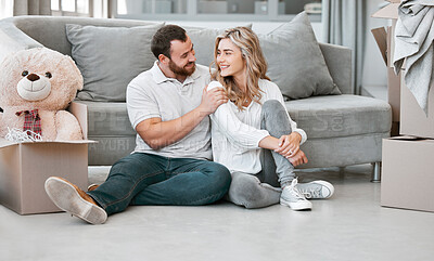 Buy stock photo Loving couple looking at each other while sitting in their new home. Young married couple looking happy while sitting on living room floor in their new apartment. First time homeowners 