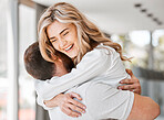 Beautiful woman hugging husband while smiling in their home. Young wife hugging her man while standing in the living room. Feeling happiness and love and showing affection. Husband and wife embracing