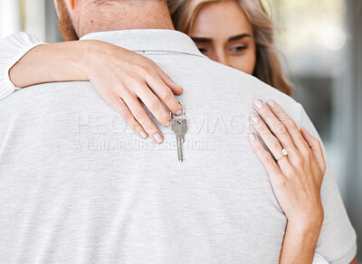 Closeup of happy wife hugging husband while holding keys after buying first home. Couple relocating to new house or apartment. Newlywed couple moving into their new place