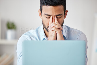 Young mixed race businessman suffering from headache while working on a laptop in an office alone at work. One hispanic man feeling stressed while working. Male boss looking unhappy sitting at a desk