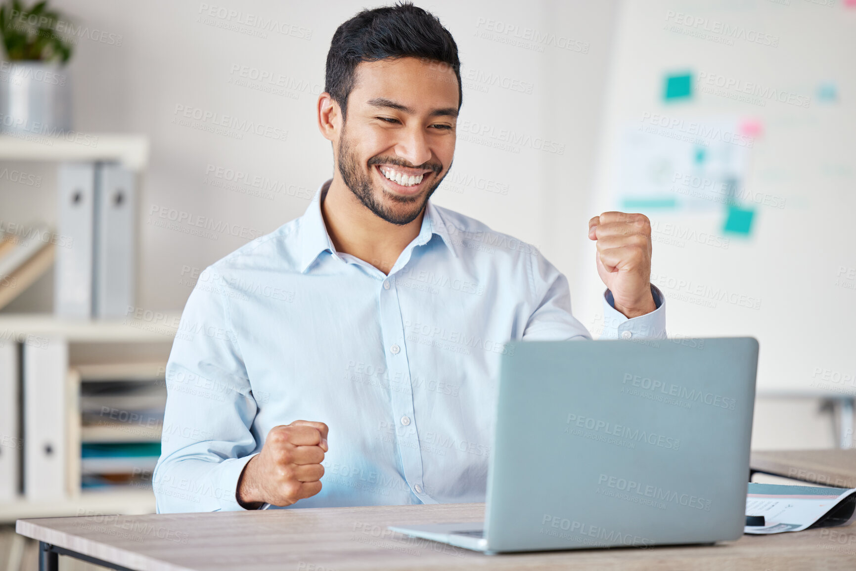 Buy stock photo Young happy and excited mixed race businessman cheering with his fist while working on a laptop alone in an office at work. One hispanic male boss smiling while celebrating success