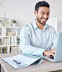 Young happy mixed race businessman working on a laptop alone in an office at work. One hispanic male boss smiling while typing an email and using a report sitting at a desk