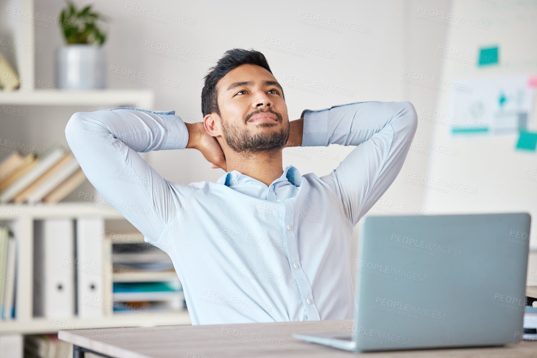Buy stock photo Young mixed race businessman resting with his arms behind his back working on a laptop in an office at work. Hispanic man relaxing while thinking. Male boss enjoying success alone at work